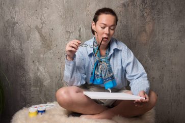 Woman sitting and looking on canvas with brush on marble background
